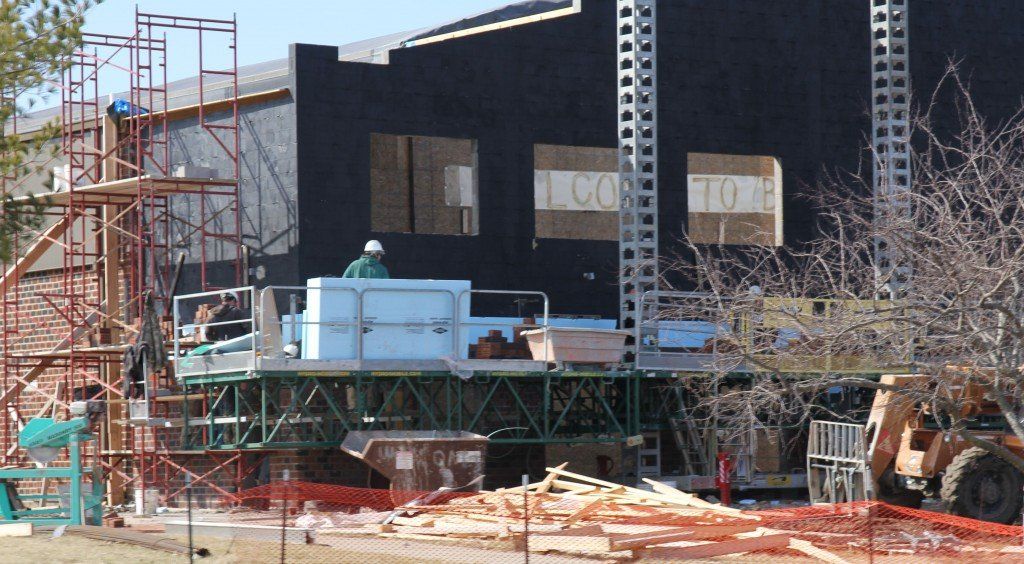 Workers face the front of the high school gym with brick. They also connected the new wall to the existing roof. 