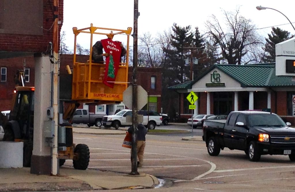 Workers for the City of Gillespie hang the holiday banners and decorations in downtown last week. The holiday lights light up the street at night. 
